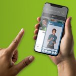 Mão com o indicador esticado se aproxima da tela de celular exibindo o site da Cross Content e, sobre ele, em parte da tela, o aplicativo da Rybená com o desenho em animação 3D da personagem que faz a leitura de libras